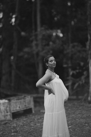 A person in a flowing white dress poses expressively in a dark outdoor setting.