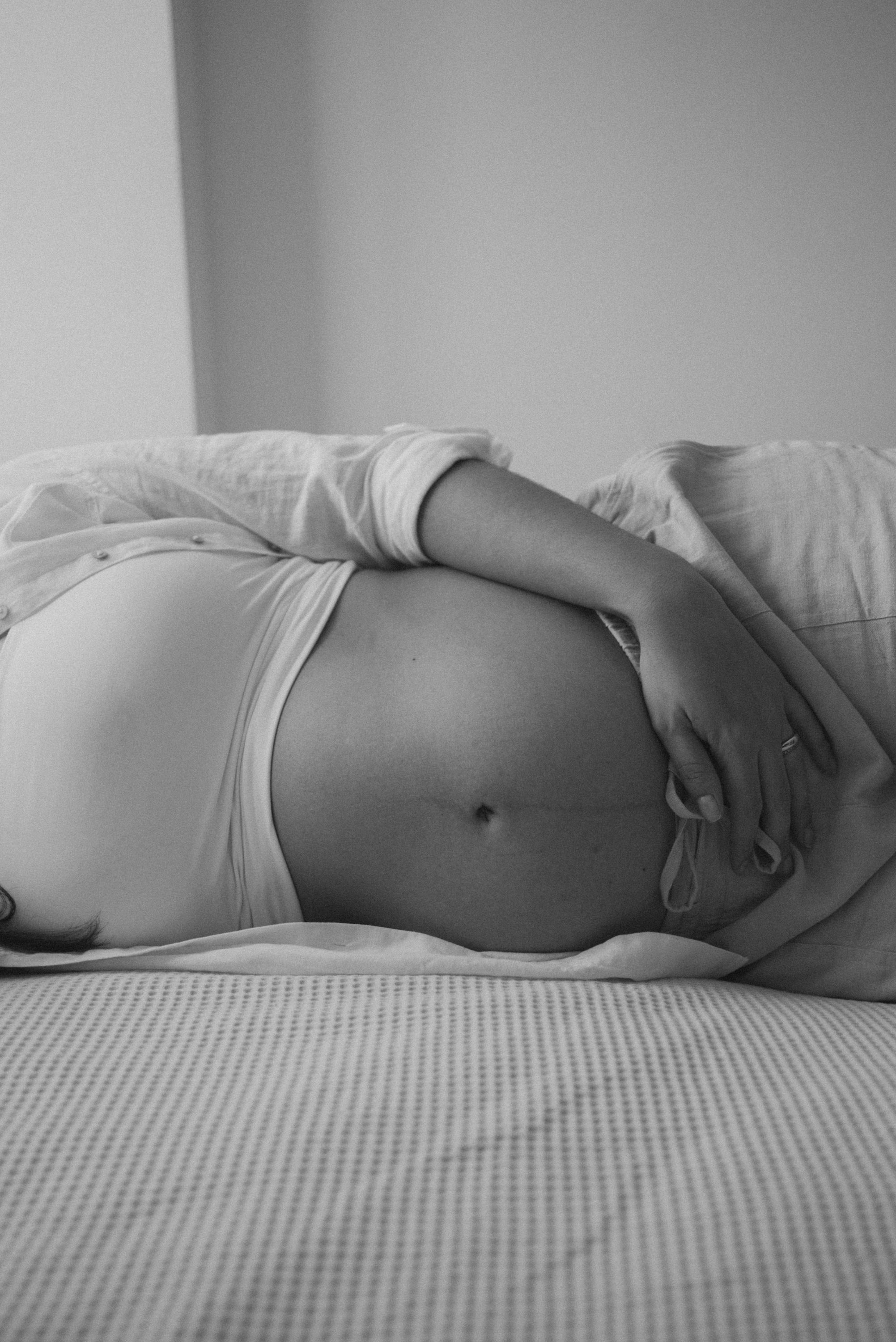 Intimate black and white photograph of pregnant belly with hands resting gently on top.