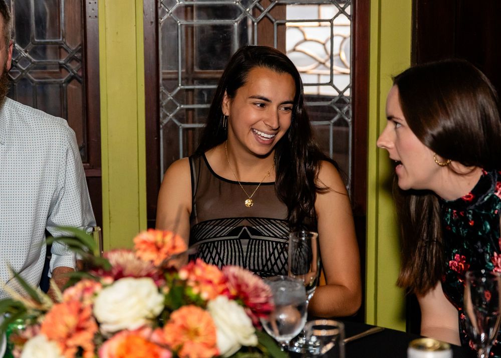 Two women smiling and conversing at an elegant dinner event with floral centerpiece.