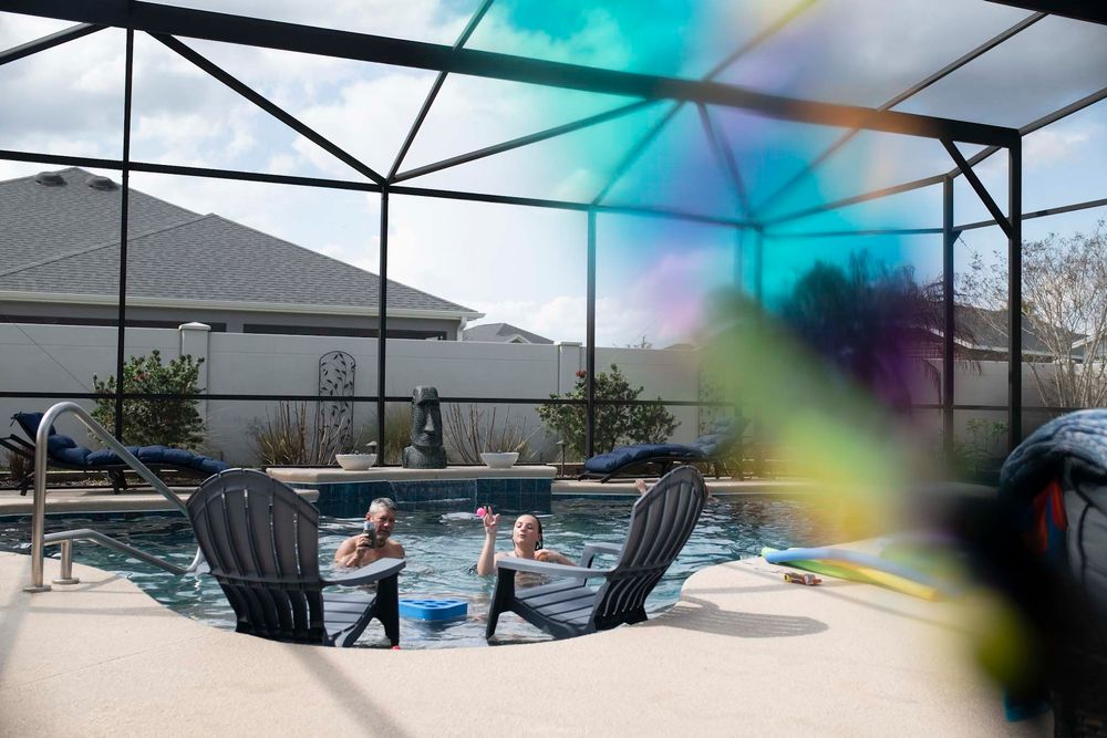 Two people enjoying a screened pool patio on a sunny day, with a colorful bubble floating in the foreground.