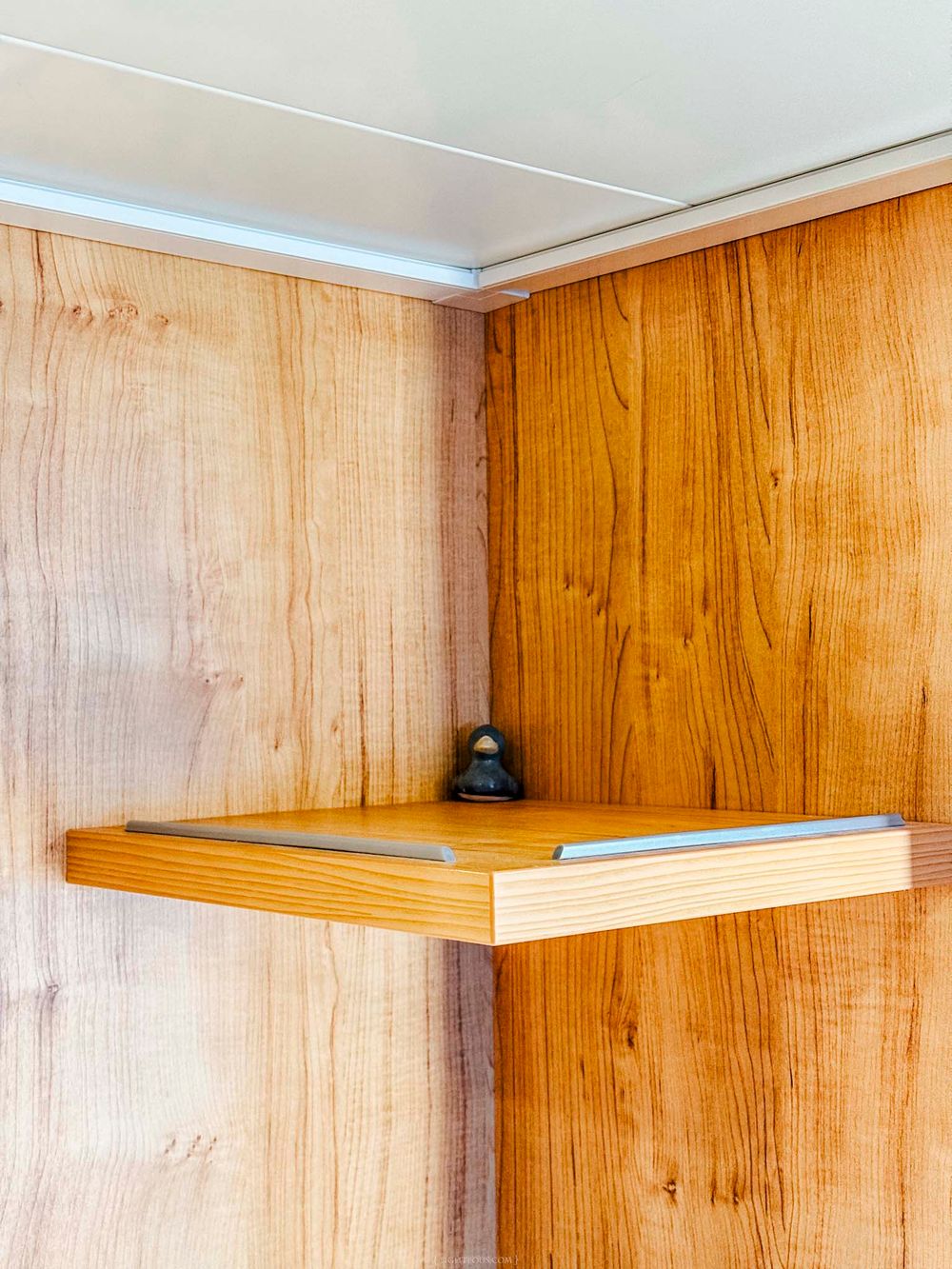 A wooden corner shelf mounted inside a cabinet with light wood grain panel walls.