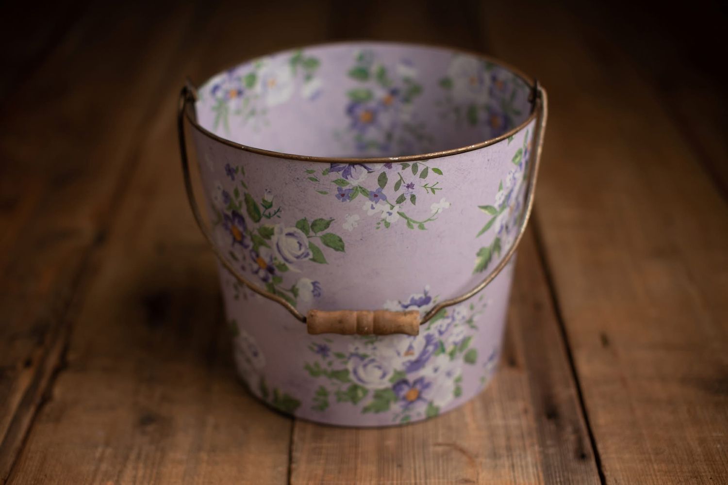 Vintage floral pink bucket with bamboo handle featuring purple flowers and green leaves on rustic wooden surface.