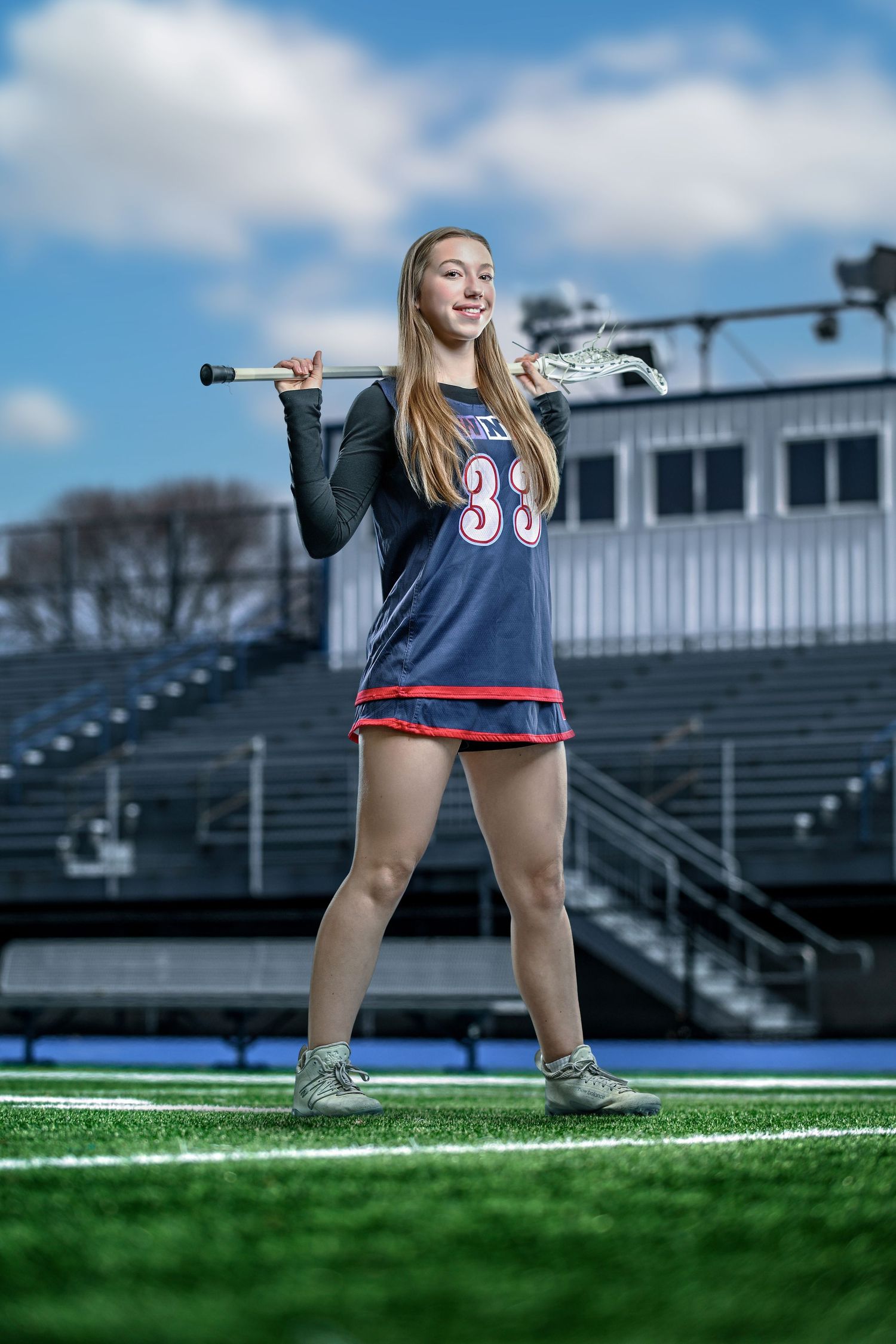 Female lacrosse player #39 posing with stick on athletic field with stadium bleachers in background.