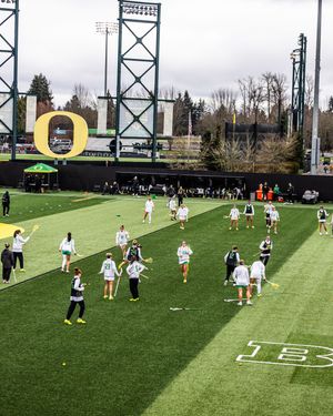 University of Oregon women's lacrosse team warming up on green turf field with iconic O logo visible.