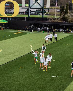 Oregon Ducks women's lacrosse team warms up on turf field with large O logo.