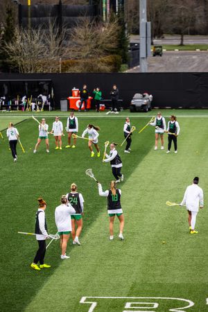 Women's lacrosse team warming up on green turf field during practice session.
