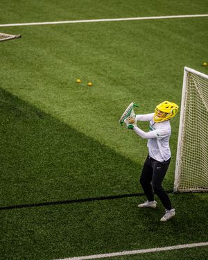 Lacrosse goalie in yellow helmet practices saves near goal on green turf field during training.