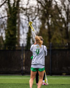 Female lacrosse player wearing number 4 raises her stick overhead on a turf field during a game.