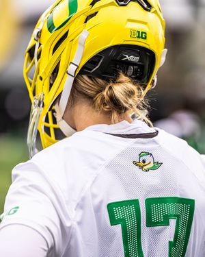 Back view of Oregon Ducks lacrosse player wearing yellow helmet and white jersey number 17 with duck logo.