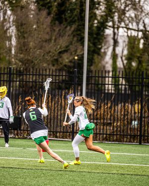 Oregon Ducks women's lacrosse players in green uniforms competing during a game on turf field.