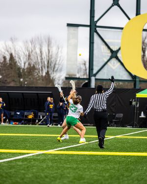 Oregon Ducks women's lacrosse player shoots as referee signals during a college game.