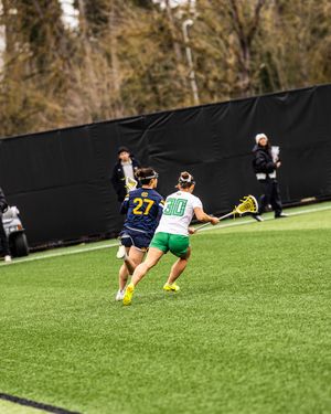 Female lacrosse players number 27 and 10 competing on turf field during game.