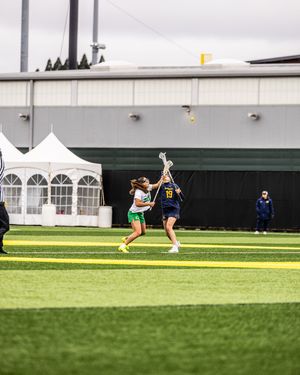 Two female lacrosse players compete for the ball on a green turf field during a game.