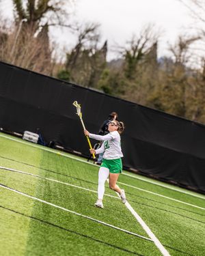 Female lacrosse player in green and white uniform runs along turf field while cradling ball in her lacrosse stick.