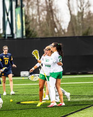 Two Oregon Ducks women's lacrosse players celebrate on the field during a game against California.