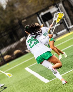 Oregon Ducks women's lacrosse player number 29 sprints down the turf field carrying a lacrosse stick.