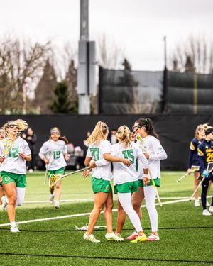 Oregon Ducks women's lacrosse team huddles on field in green and white uniforms.