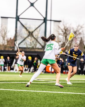 Female lacrosse player wearing number 25 prepares to shoot during a competitive college game on turf field.