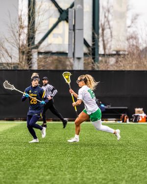 Oregon Ducks women's lacrosse player dodges Cal defender during college game on turf field.