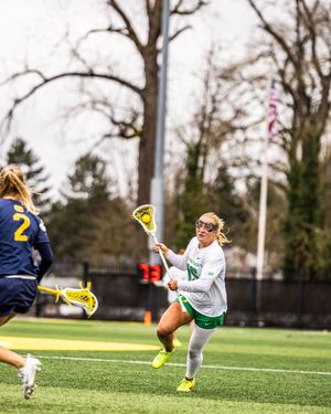 Oregon Ducks female lacrosse player in green uniform cradles the ball during a college game on turf.
