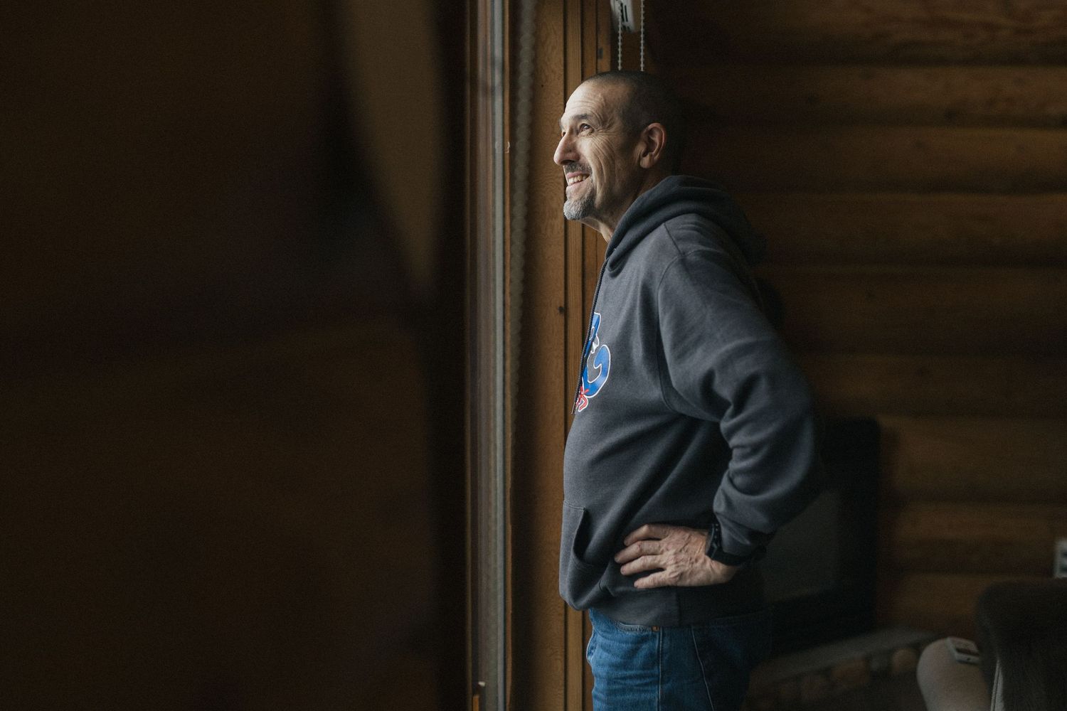 groom smiles as he looks out the window of log cabin on his wedding morning