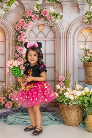 Young girl in Minnie Mouse costume with pink tutu, ears, and tulips poses before floral arch backdrop.
