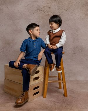 Two young boys in navy blue outfits pose on wooden crates in a professional studio portrait photo.