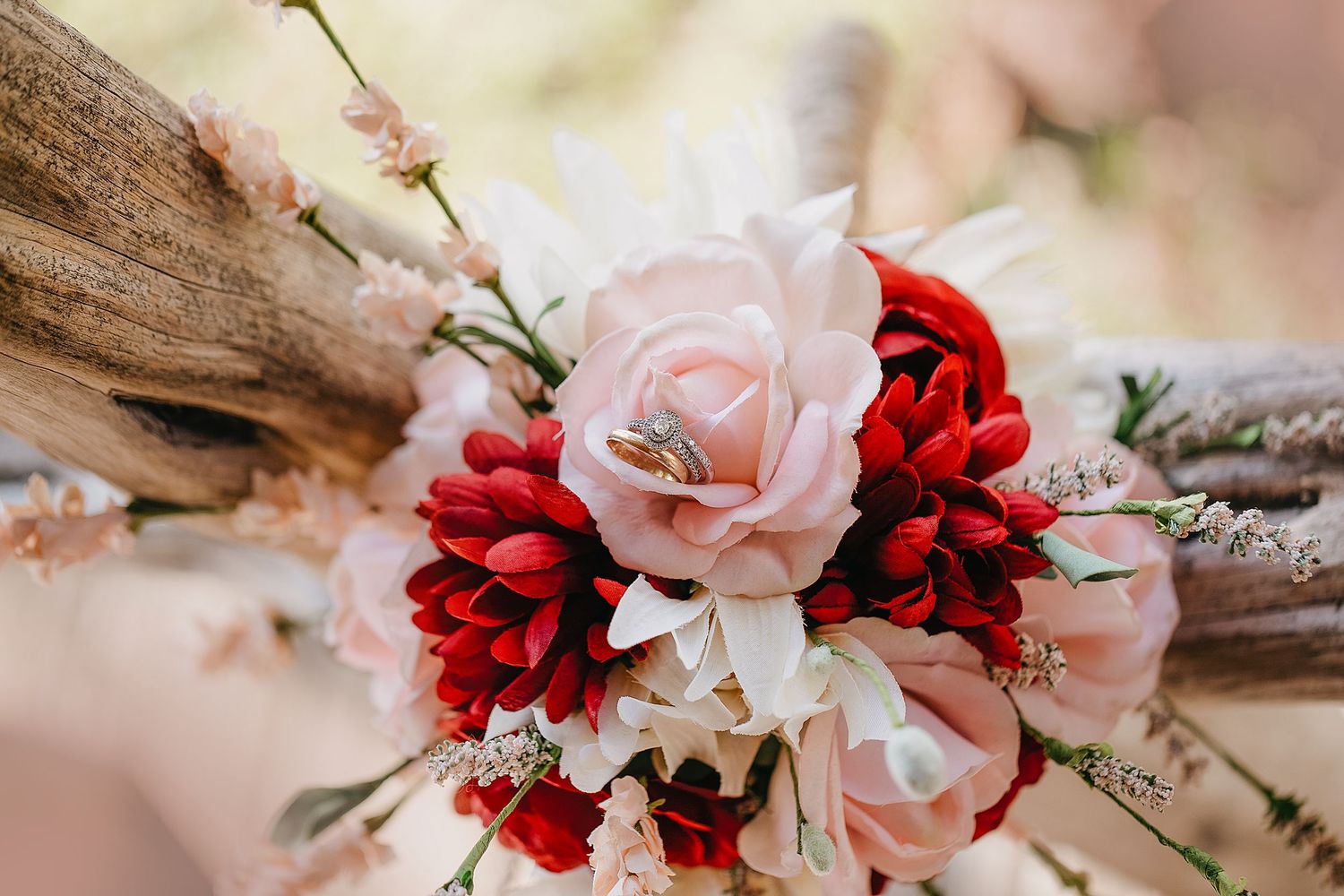 Pink and red roses with a wedding ring resting on top of a rustic wooden arrangement.