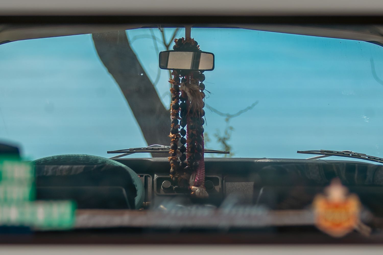 View through a car windshield showing hanging beaded rosary on rearview mirror with dashboard visible.