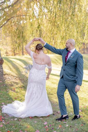 Groom in gray suit spinning bride in lace off-shoulder gown under a golden willow tree at fall wedding in Sparta, NJ.