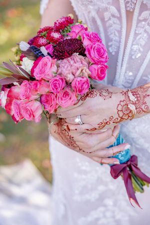 Close-up of bride holding pink rose bouquet with henna-adorned hands and diamond engagement ring.