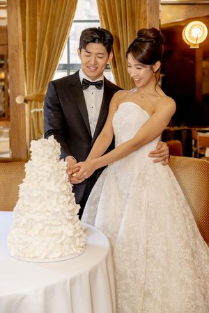 Smiling bride and groom cutting a four-tier white ruffled wedding cake at The Golden Swan Restaurant in New York City.