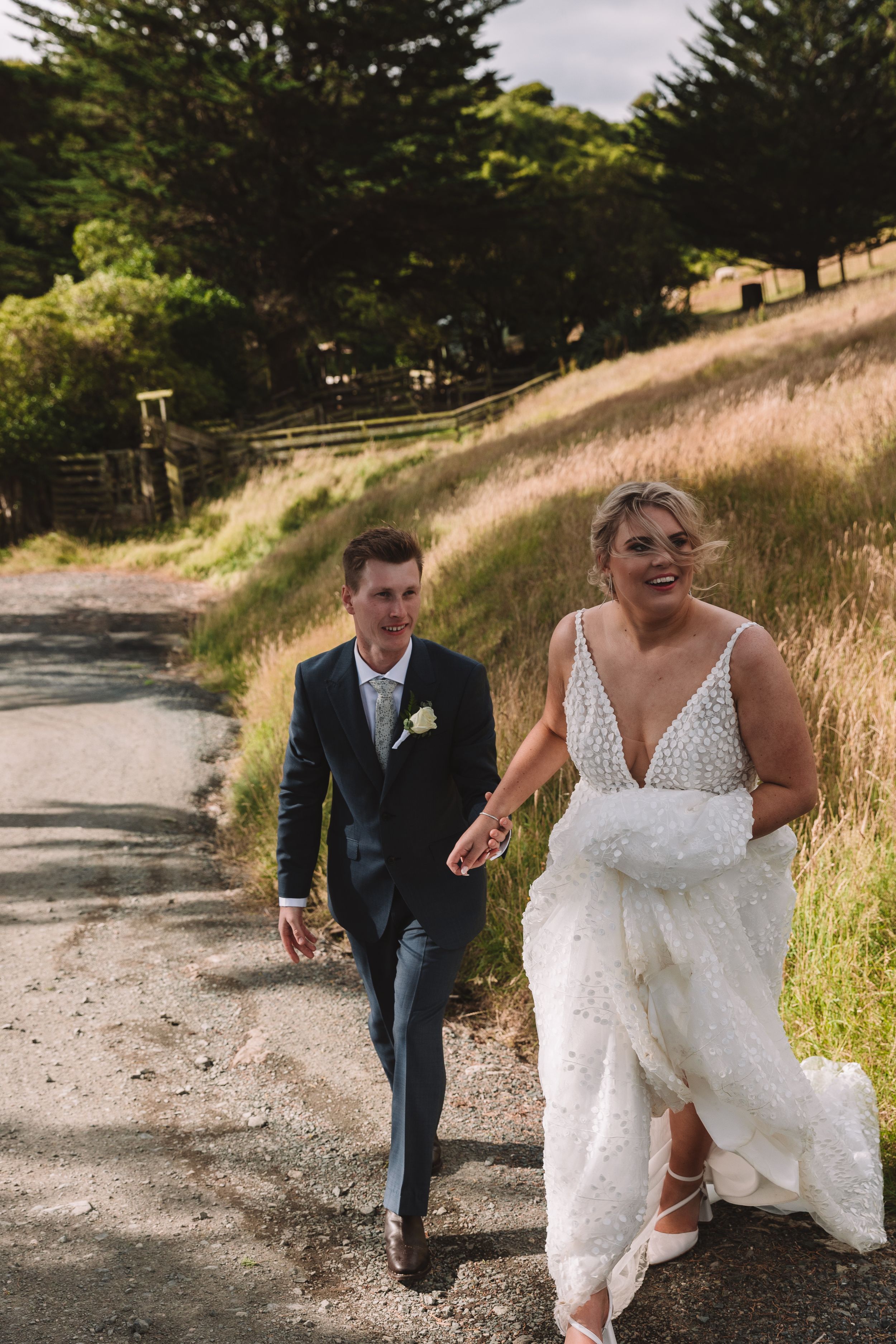 A couple walks along a winding dirt path surrounded by golden grass and pine trees.