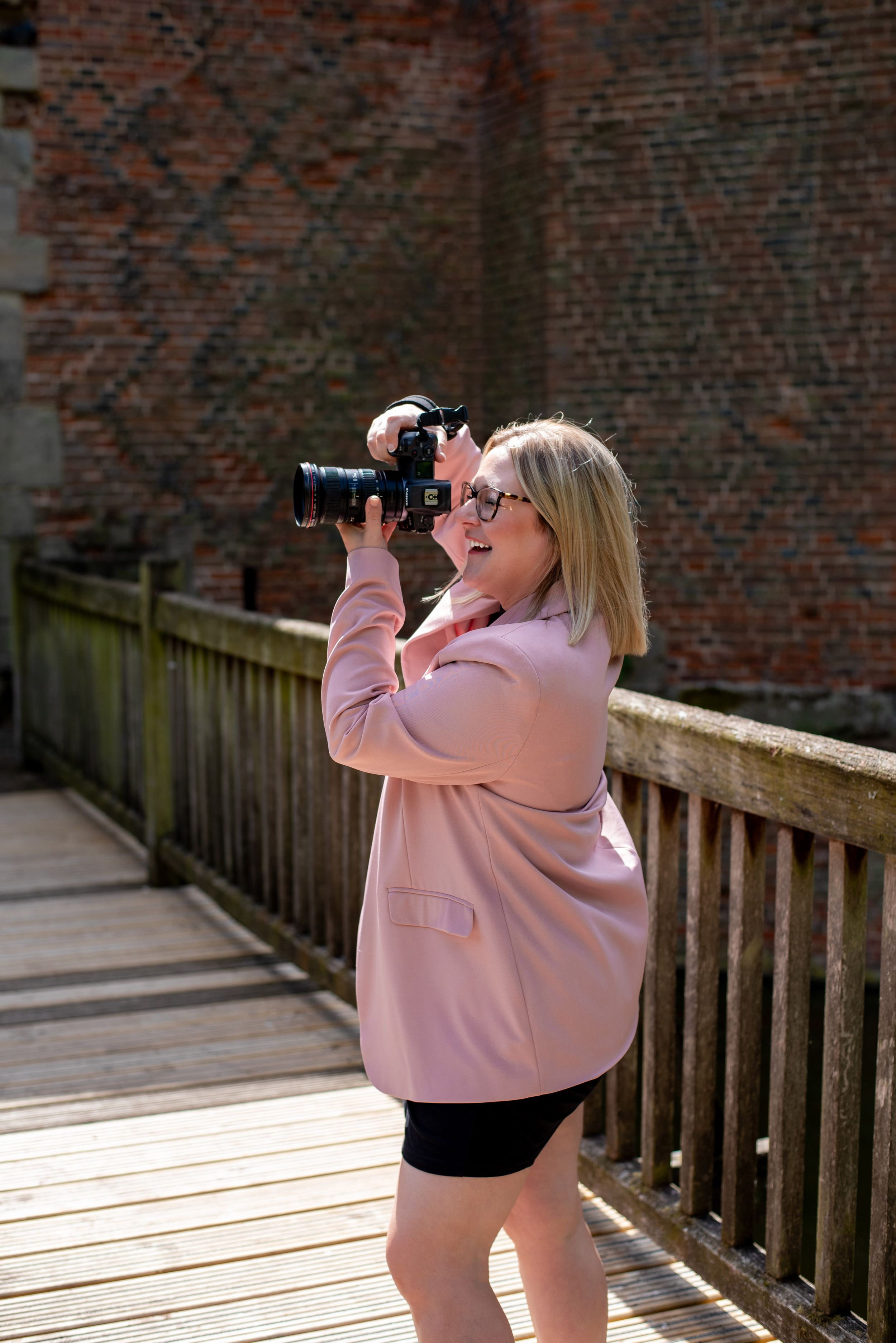 Professional photographer taking photos on wooden deck against brick wall backdrop.