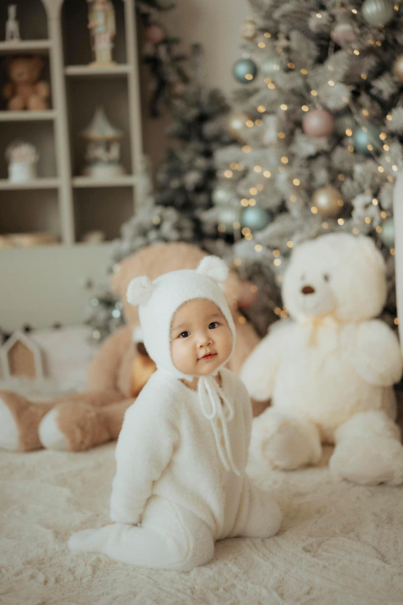 Festive holiday scene with white teddy bears and soft cozy decorations near a Christmas tree.