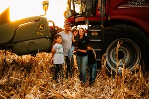 Family posing together by farm equipment in cornfield during golden hour harvest.