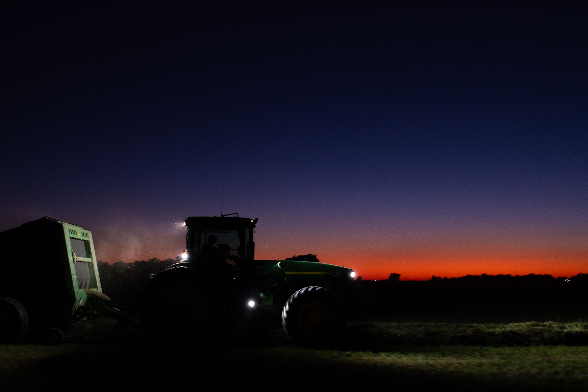 Farm tractor silhouetted against a vibrant orange and purple sunset sky.