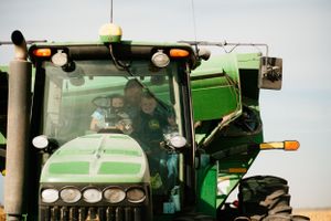 Modern green John Deere tractor cab viewed from exterior during farming operations.