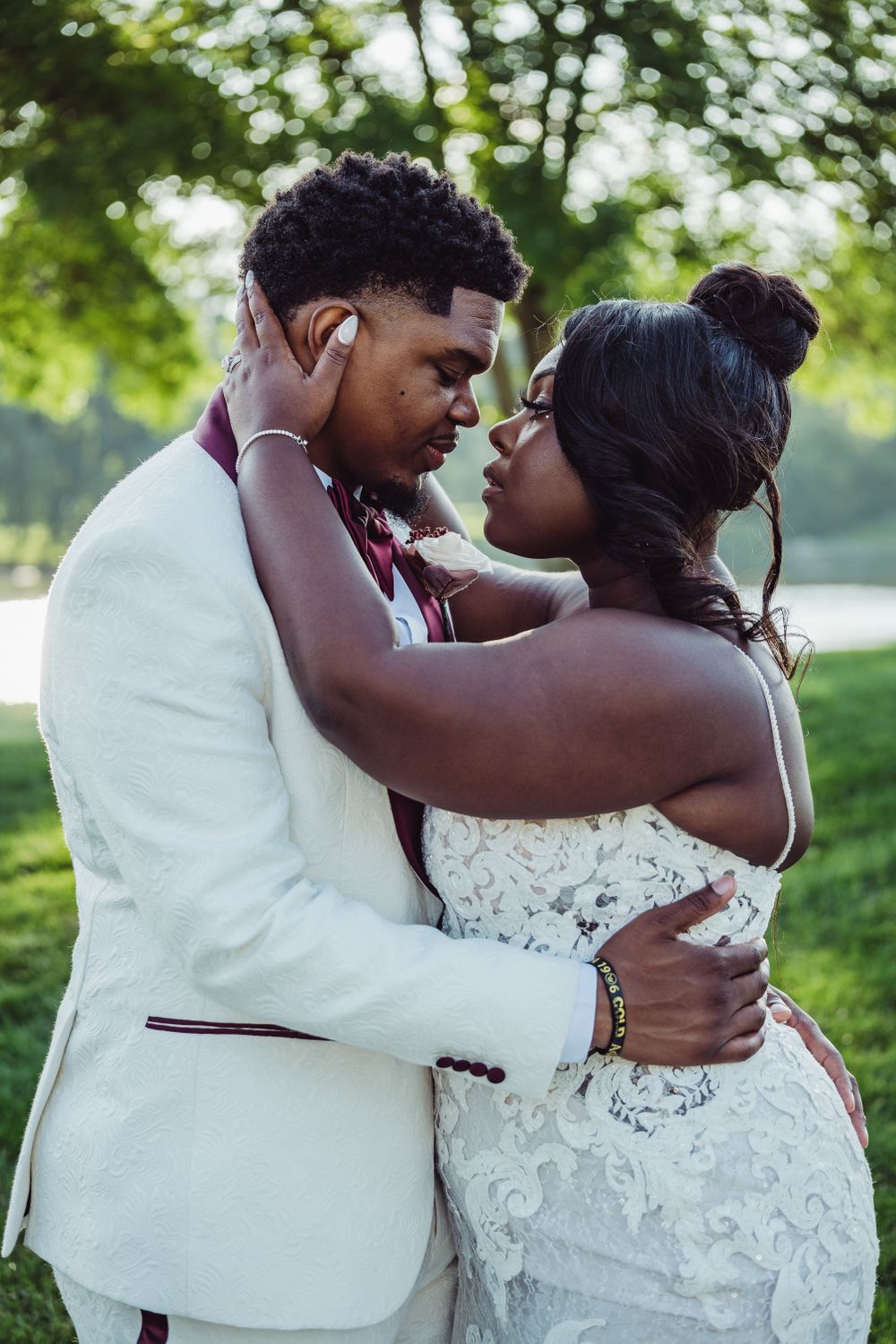 Intimate wedding portrait of couple in white attire embracing in a garden setting.