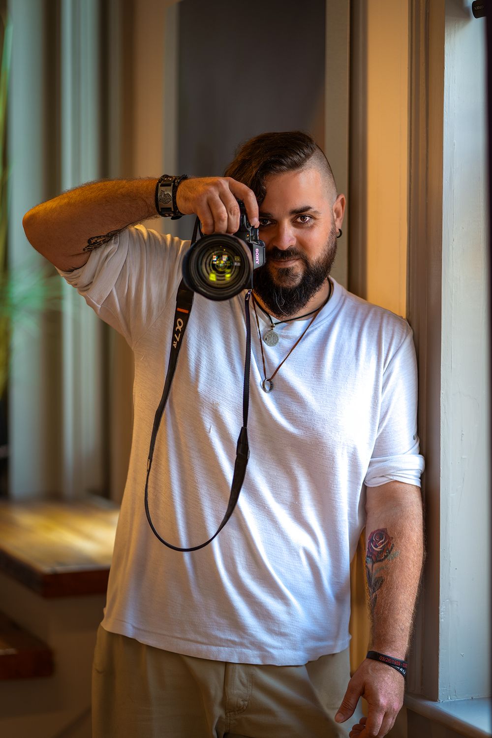 Photographer Will Shultz in a white t-shirt holds a camera near a window in natural light.