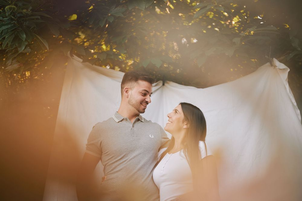 Happy couple smiling at each other outdoors with warm golden light and white fabric backdrop.