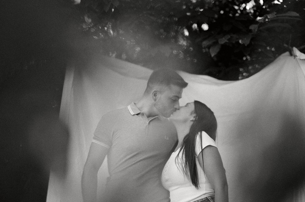 Romantic black and white photo of couple kissing outdoors with soft bokeh background.