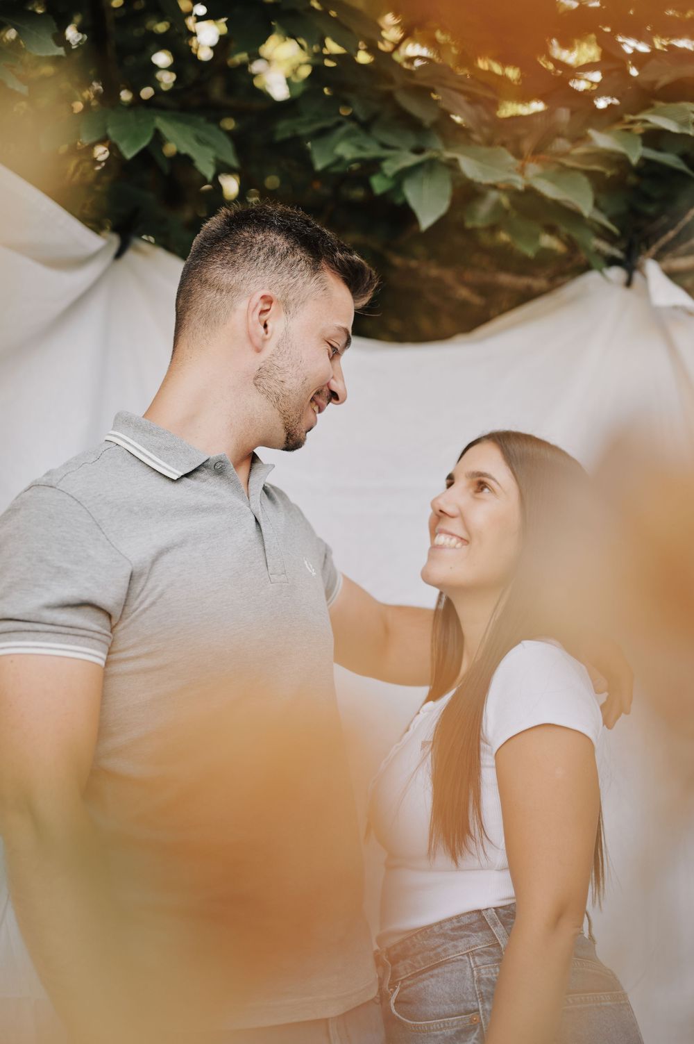 Joyful couple sharing a tender moment outdoors with lush green foliage in background.