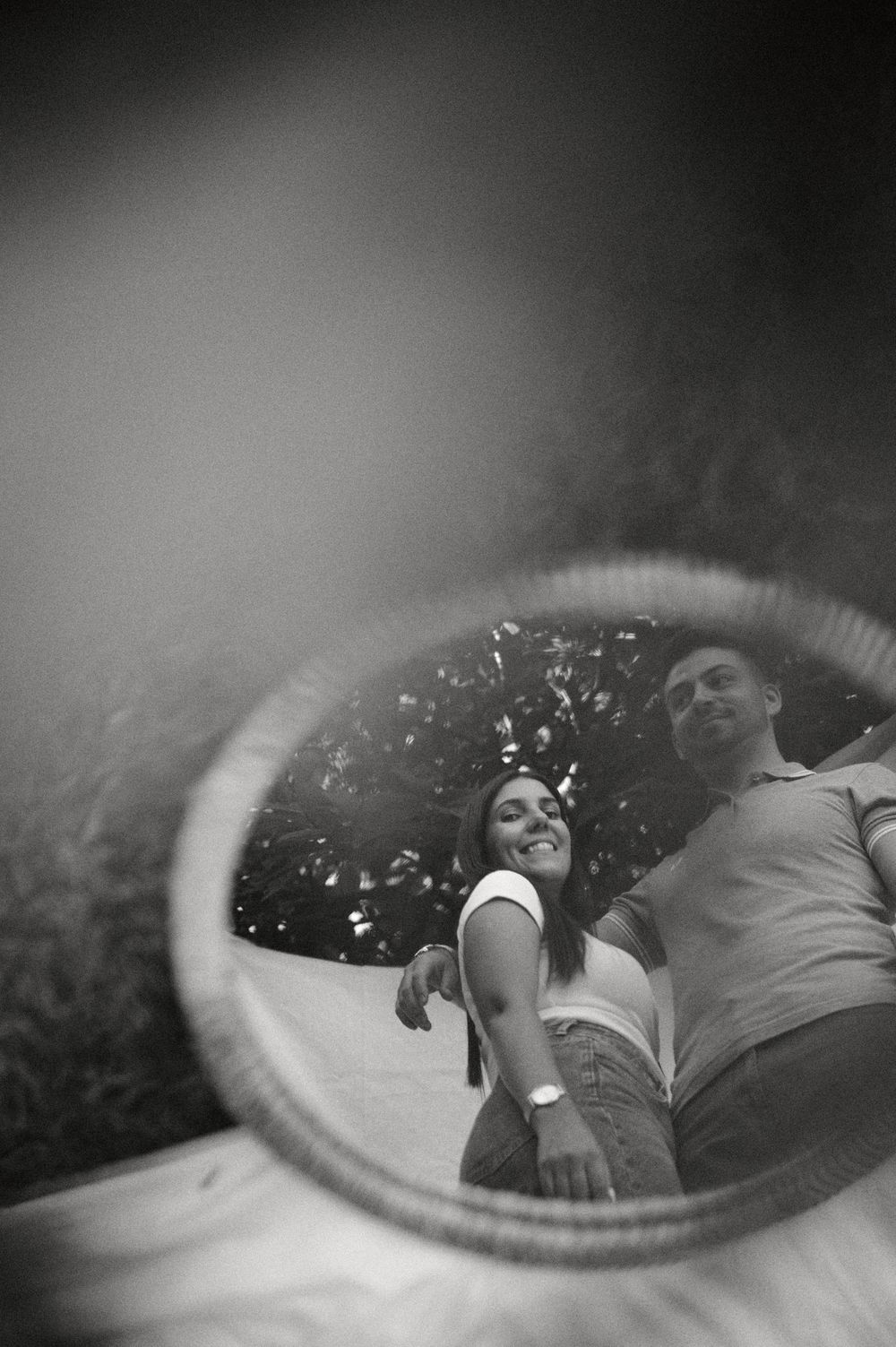 Black and white reflection of smiling couple in circular mirror with bokeh background.
