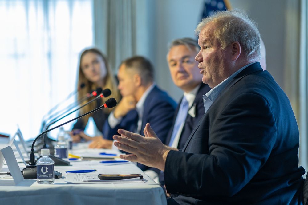 People seated at a conference table during a business meeting with microphones and documents visible.