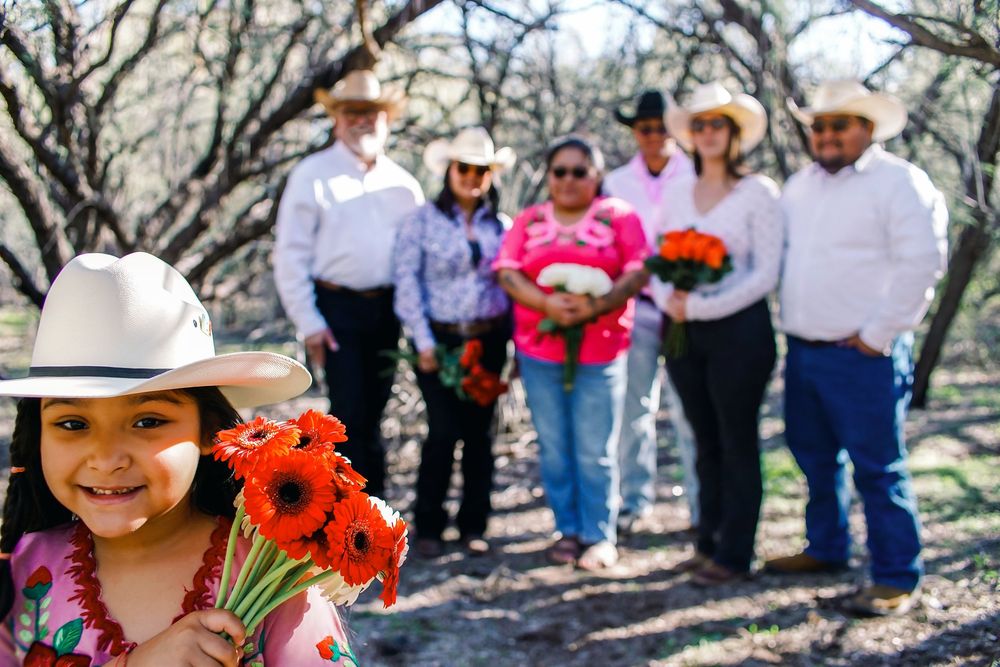 Group of people in cowboy hats and western attire walking through a blooming almond orchard in springtime.