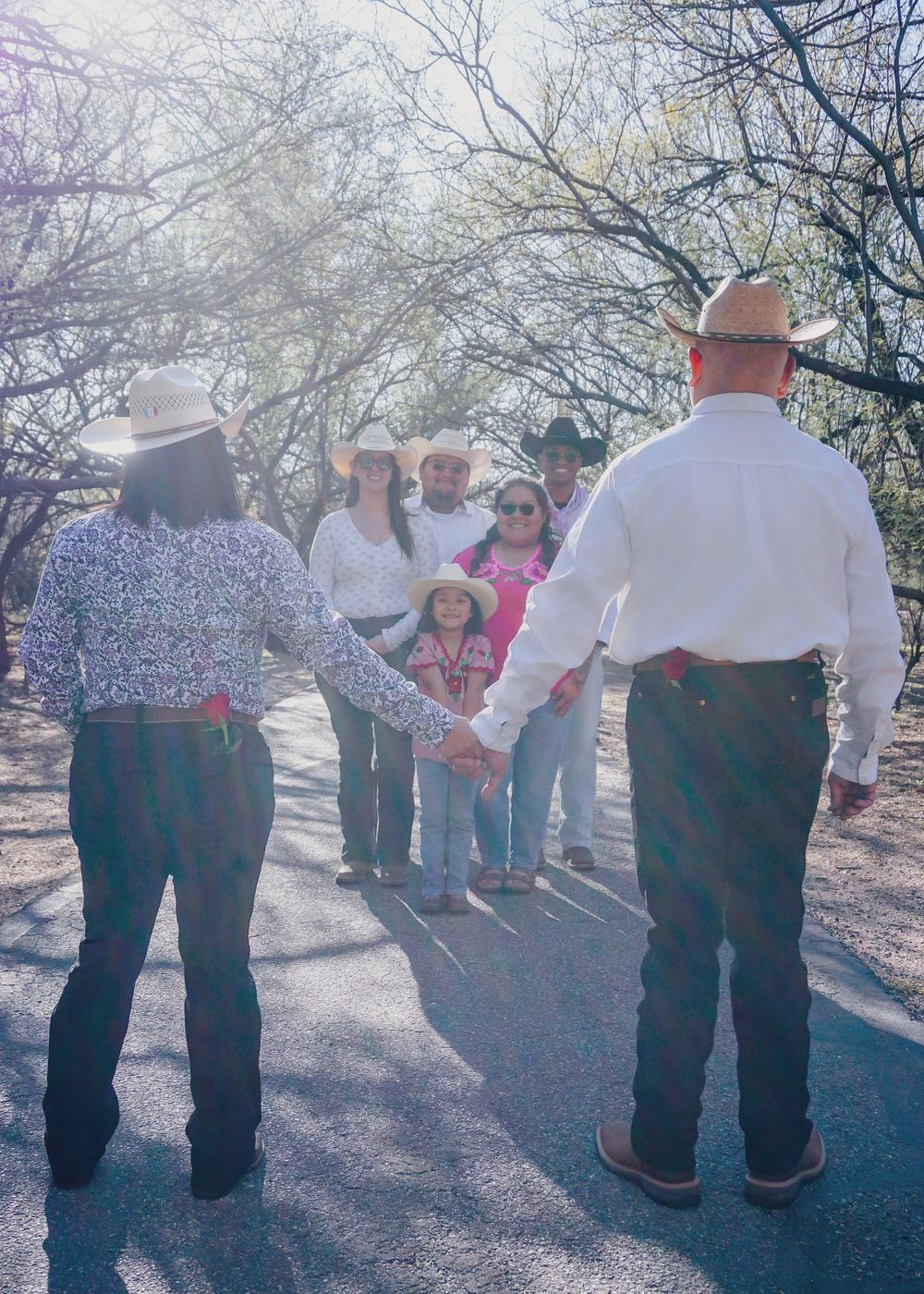 A group of people in casual attire walking along a desert trail through a grove of bare winter trees.