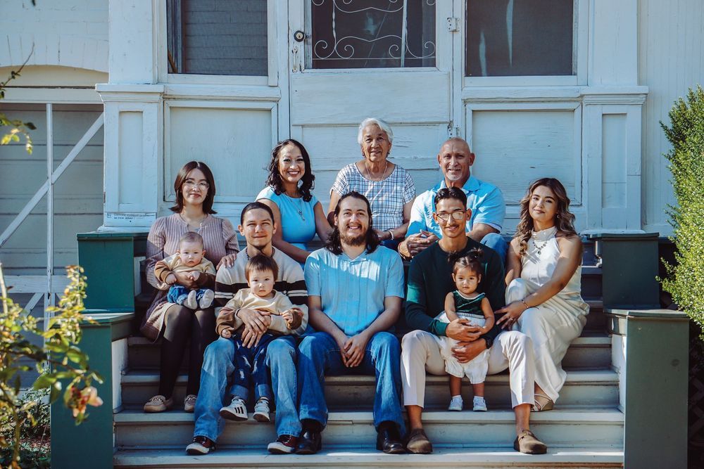 Multi-generational Latino family posing together on front porch steps of a white house for a portrait.