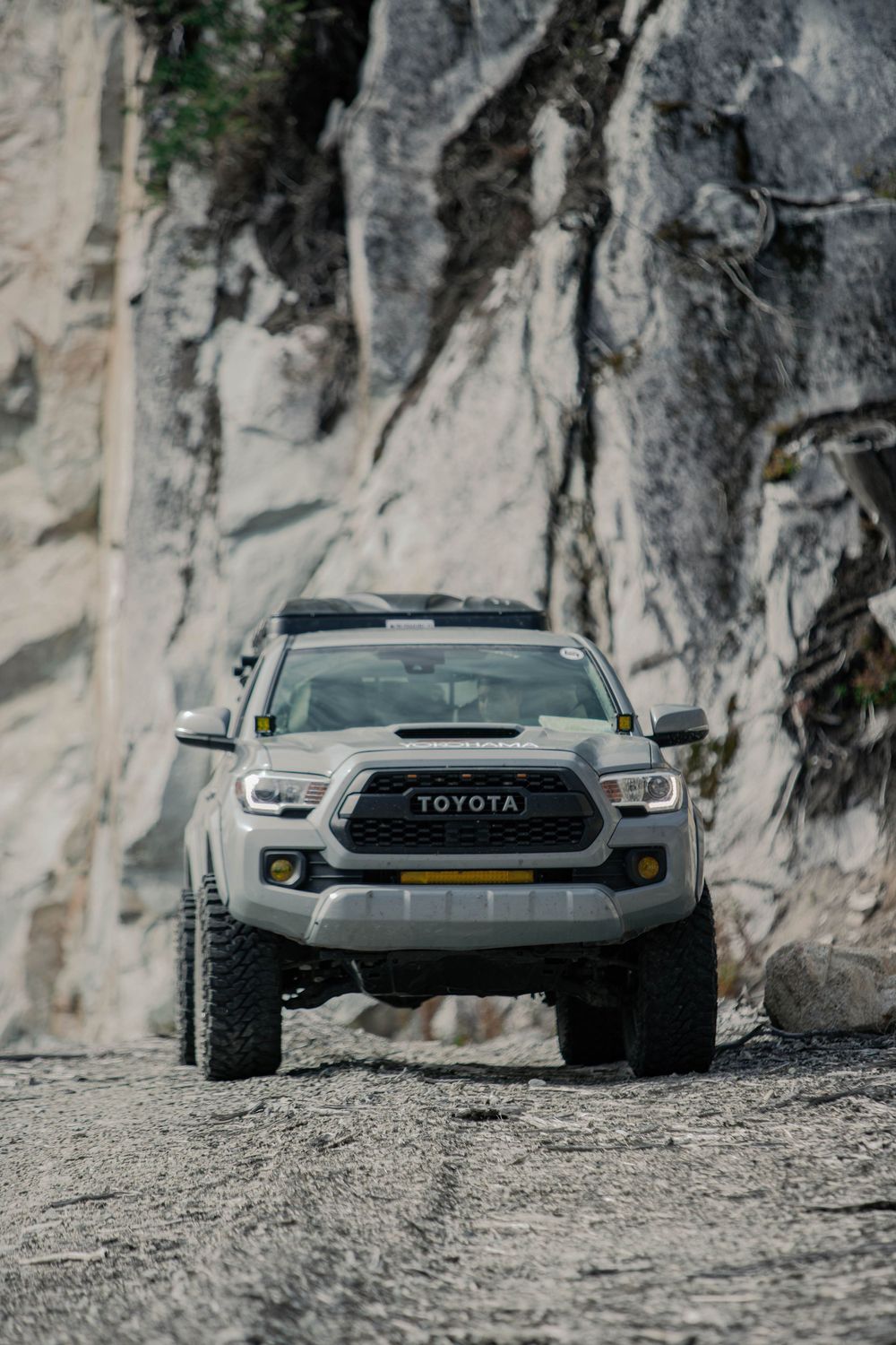 Toyota truck positioned on rocky terrain against dramatic limestone cliff face.