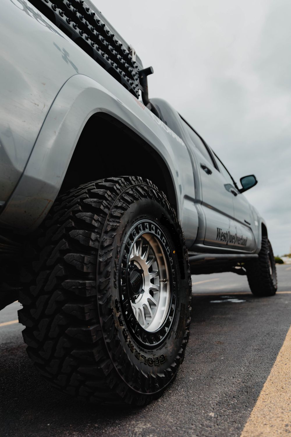 Low angle shot of a lifted silver truck with aggressive off-road tires and aftermarket wheels.